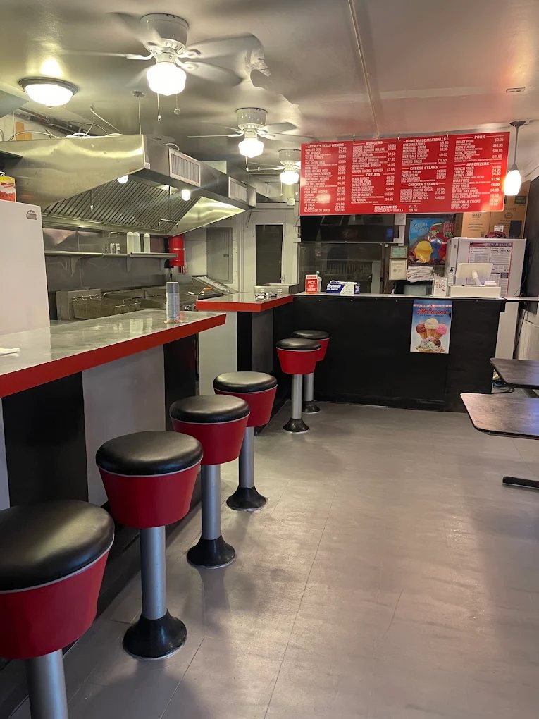 Order counter with red stools and the overhead menu board listing burgers, meatballs, pork, and cheesesteaks